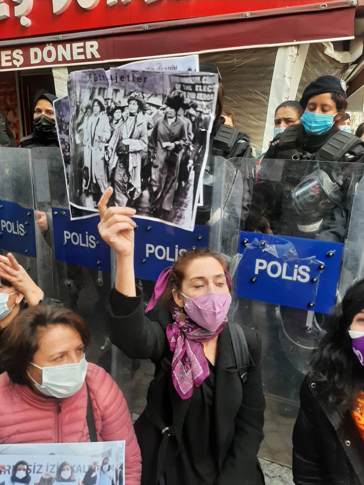 Elinde fotoğrafla oturan bir kadın, arkasında polisler