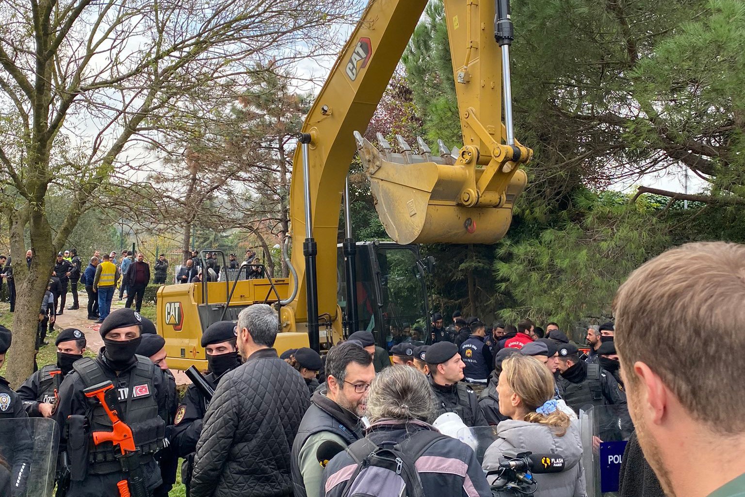 Yeşil alanda kepçe, mahalleliler ve polis.